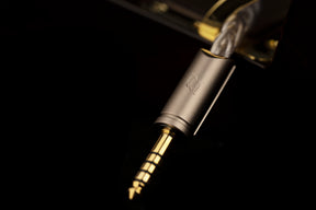 Close-up of a gold 4.4 audio jack on a black background. In-ear monitors